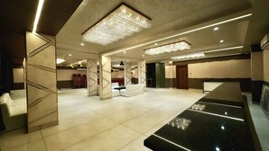 Un hall d’hôtel spacieux au design moderne, avec un grand comptoir de réception noir, d’élégants lustres et un coin salon doté de fauteuils rouges.
