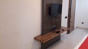 Un couloir avec un banc en bois, un téléviseur à écran plat fixé au mur et une porte à rayures verticales.