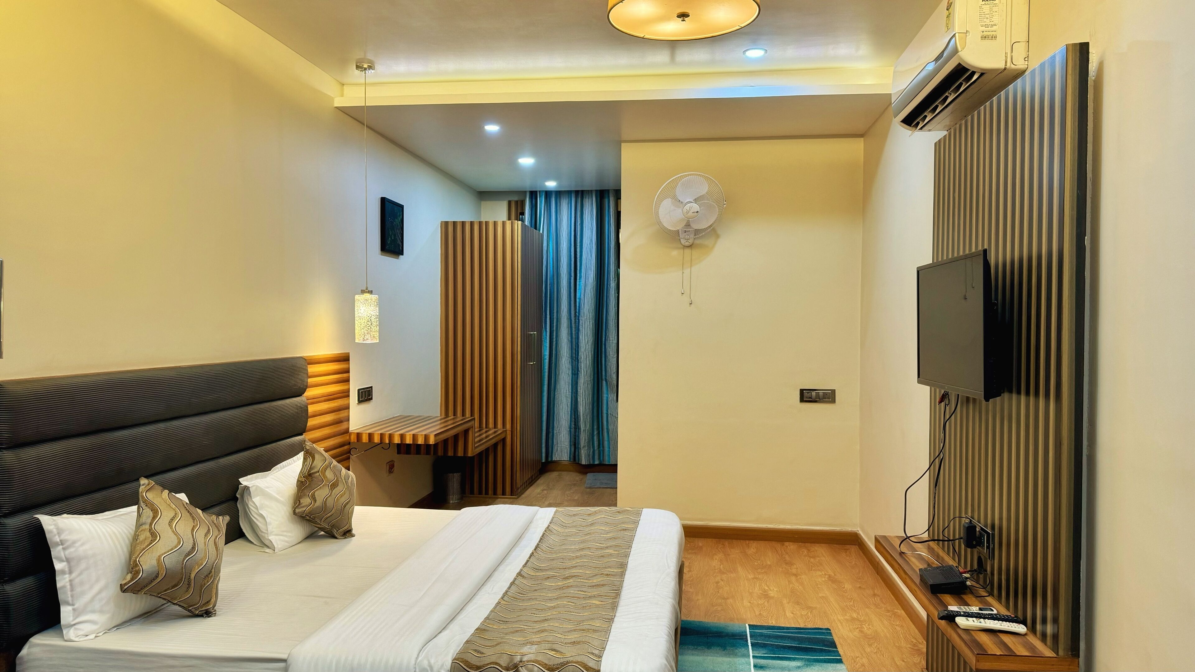 A hotel room with a bed, a desk, a television, and an air conditioning unit.