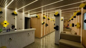 Un área de recepción con pared de paneles de madera, un mostrador de recepción y una zona de estar con sofá.