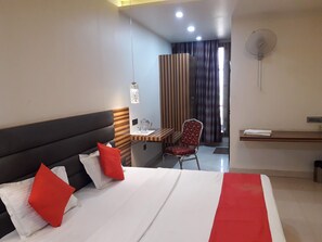 Una habitación de hotel con cama, escritorio, silla y ventilador.