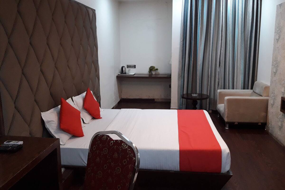 Een hotelkamer met een groot bed, een bureau, een stoel, een klein tafeltje, een bank en een gordijn.