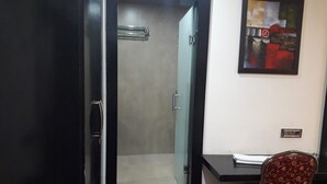Une pièce avec une porte fermée, un espace douche, un bureau avec une chaise et un tableau accroché au mur.
