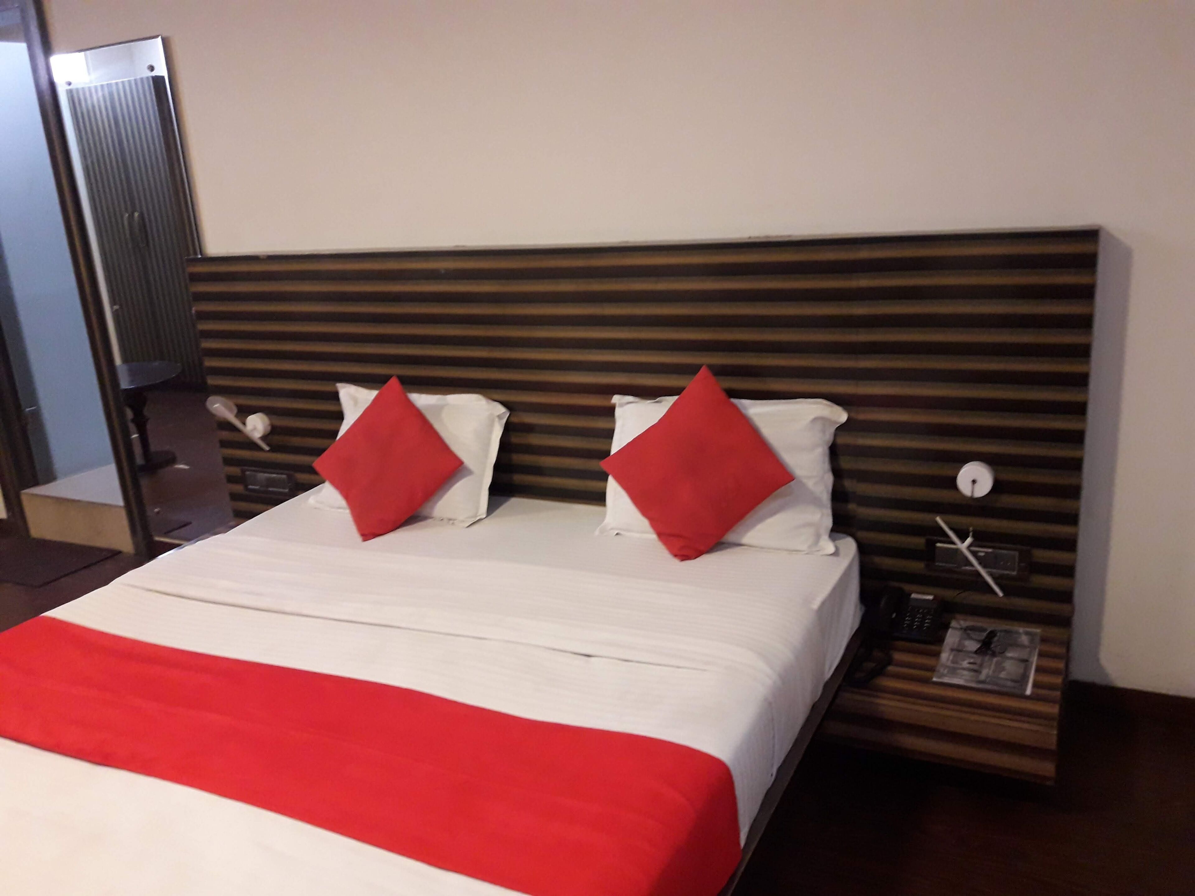 A hotel room with a bed, two red pillows, a white bedspread, and a wooden headboard.