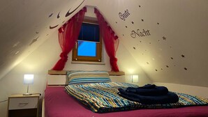 Une chambre à coucher avec un lit, une table de chevet, une fenêtre avec des rideaux rouges et des autocollants en forme d’étoiles sur le mur.