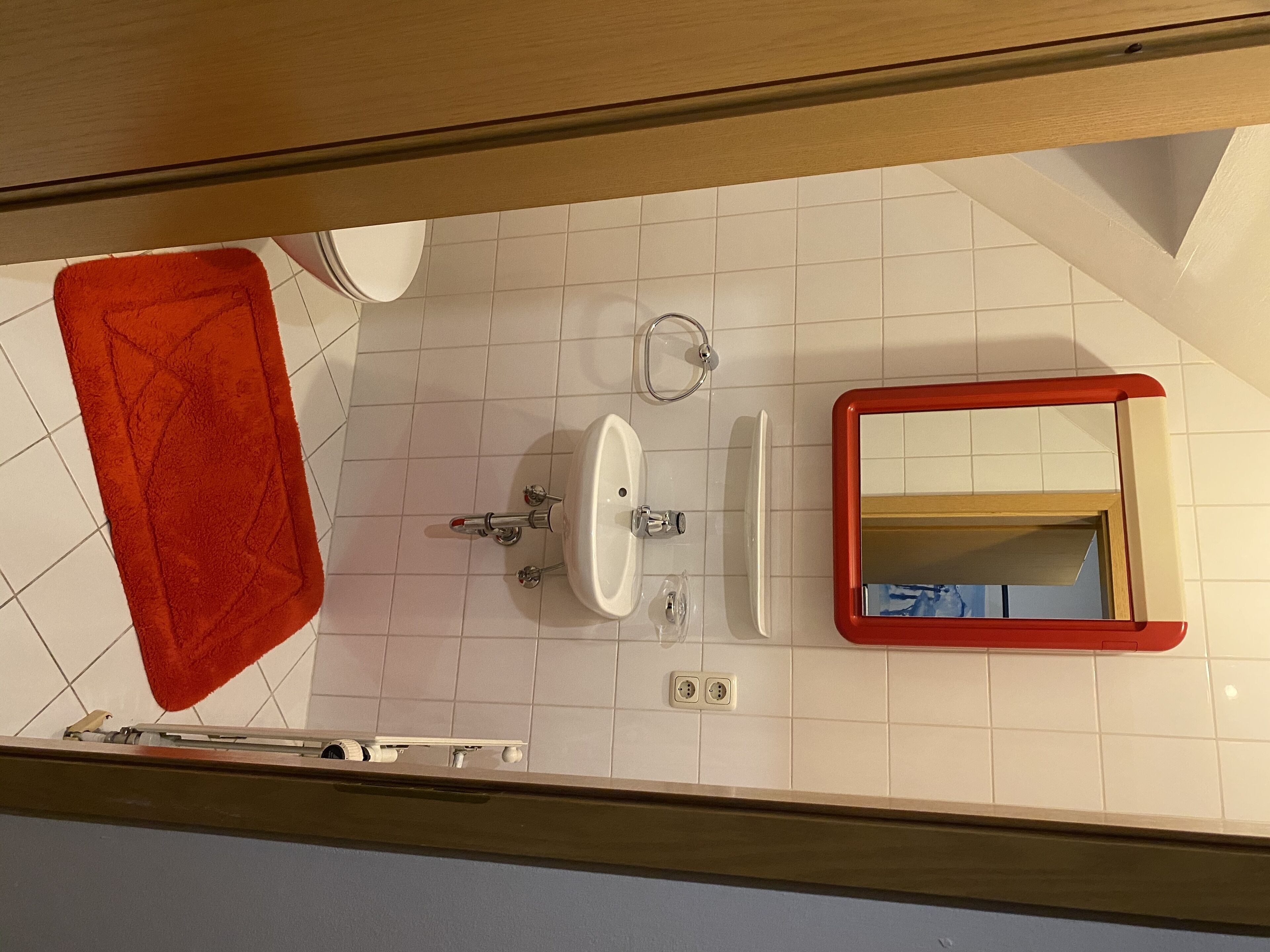 A bathroom with a white sink, a mirror, and a red bath mat.