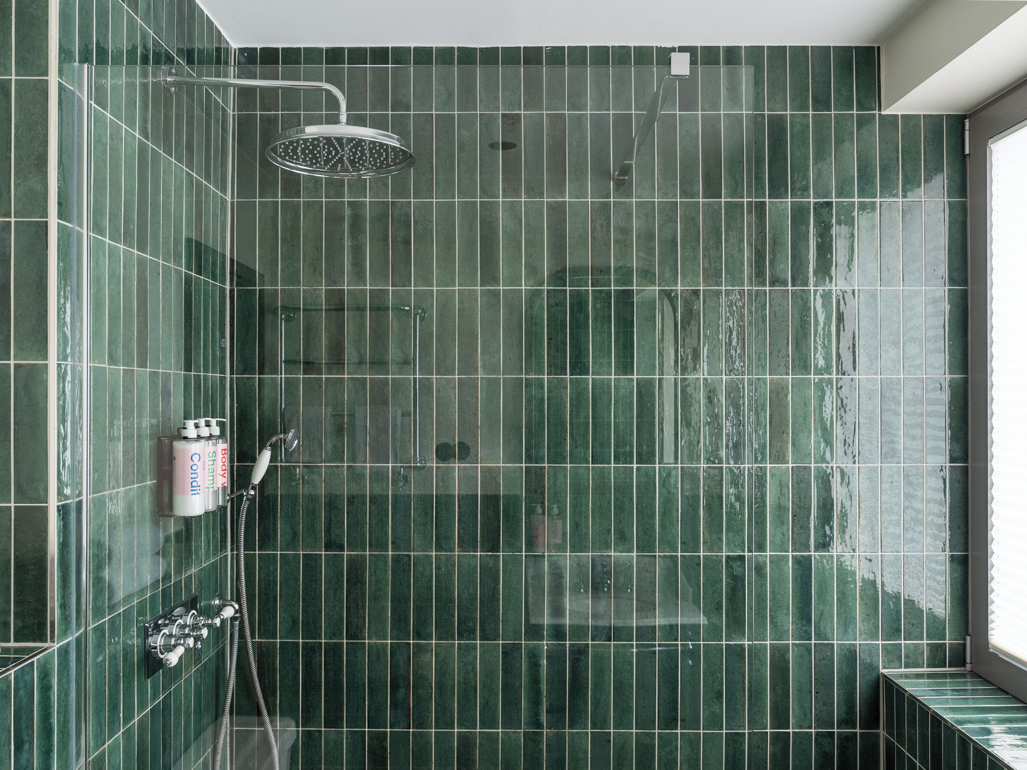A bathroom with green tiles, a shower, and a toilet.