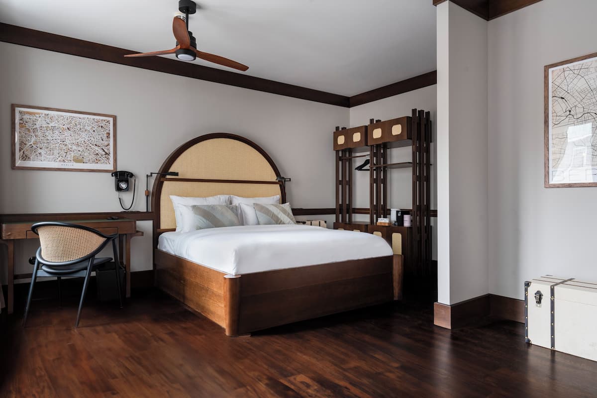 A bedroom with a wooden bed, a desk with a chair, a ceiling fan, and two framed maps on the walls.