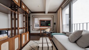 Una habitación de hotel moderna con un ventanal grande, un sofá, un escritorio con una silla y un armario de madera.