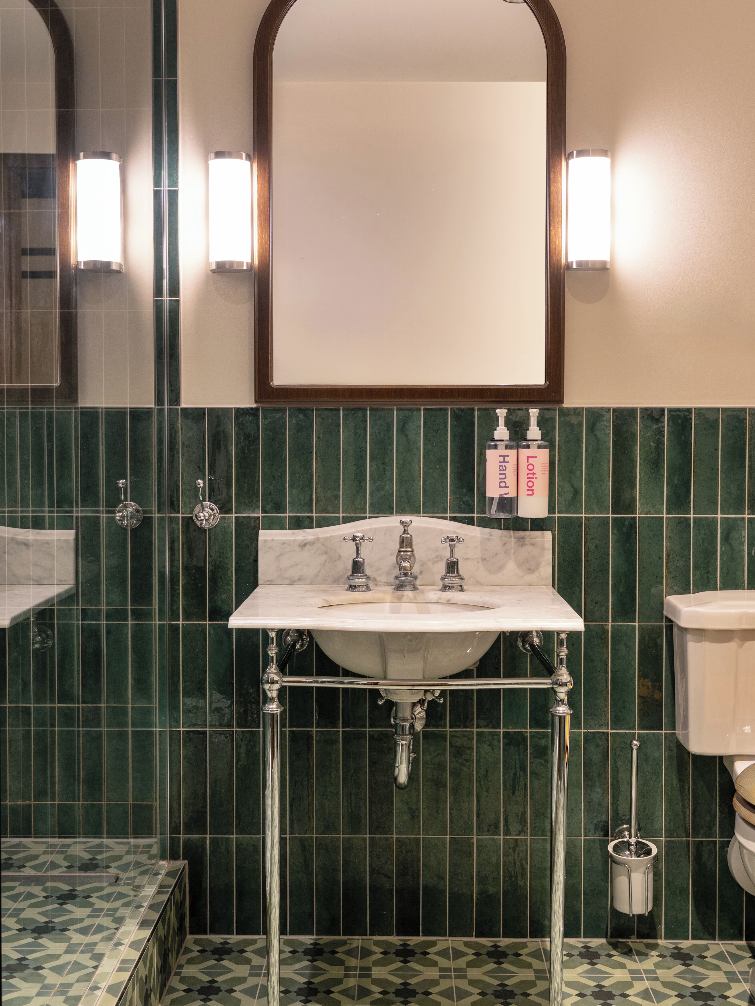 Un baño con un lavabo blanco, paredes con azulejos verdes y un espejo sobre el lavabo.