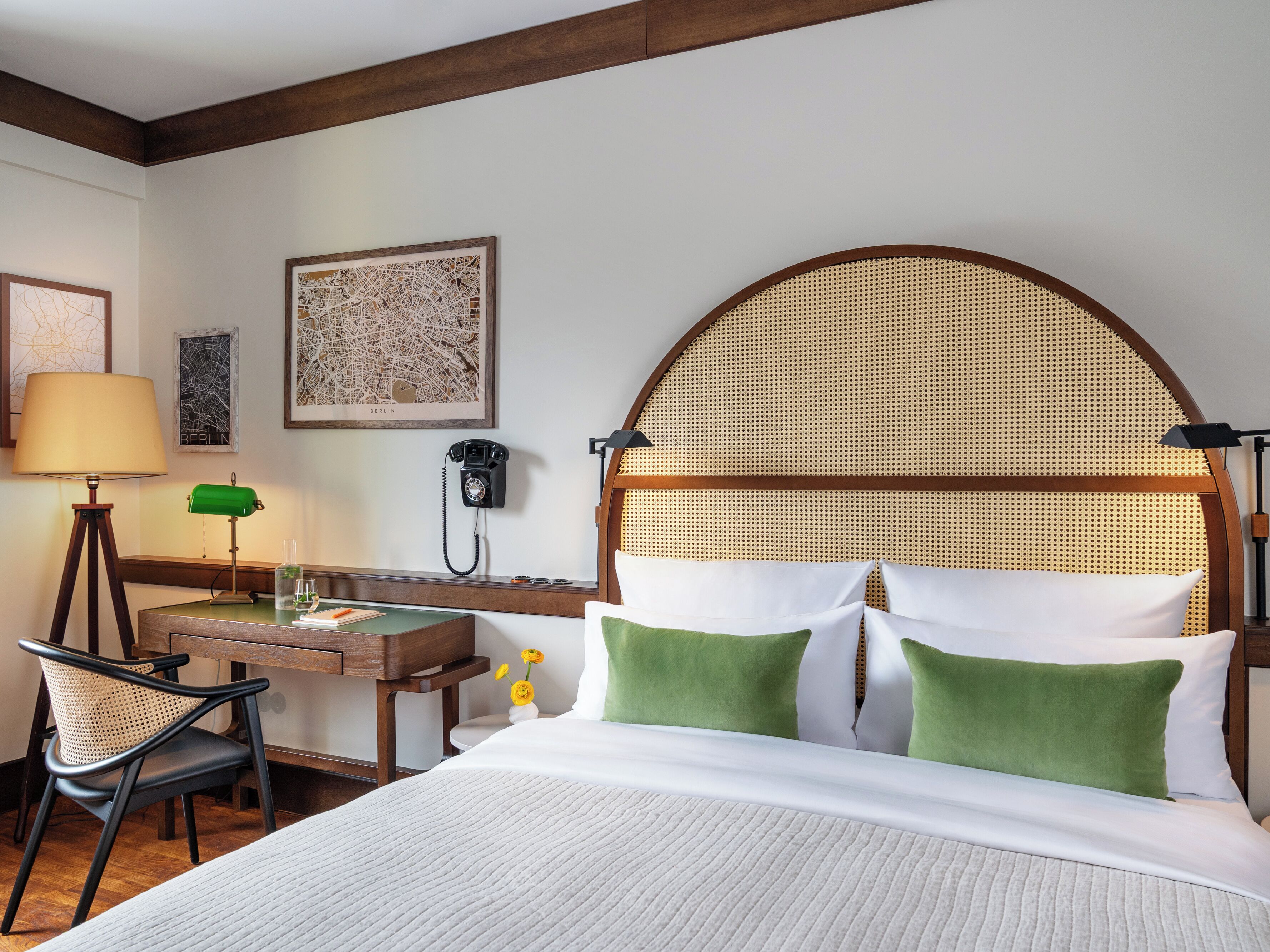 A hotel room with a bed, desk, chair, lamp, and a wall-mounted telephone.