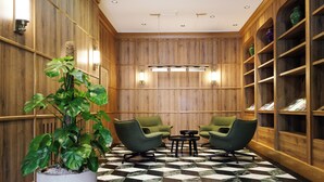 Un vestíbulo con paneles de madera, piso a cuadros, sillas verdes, una planta en maceta y una estantería.