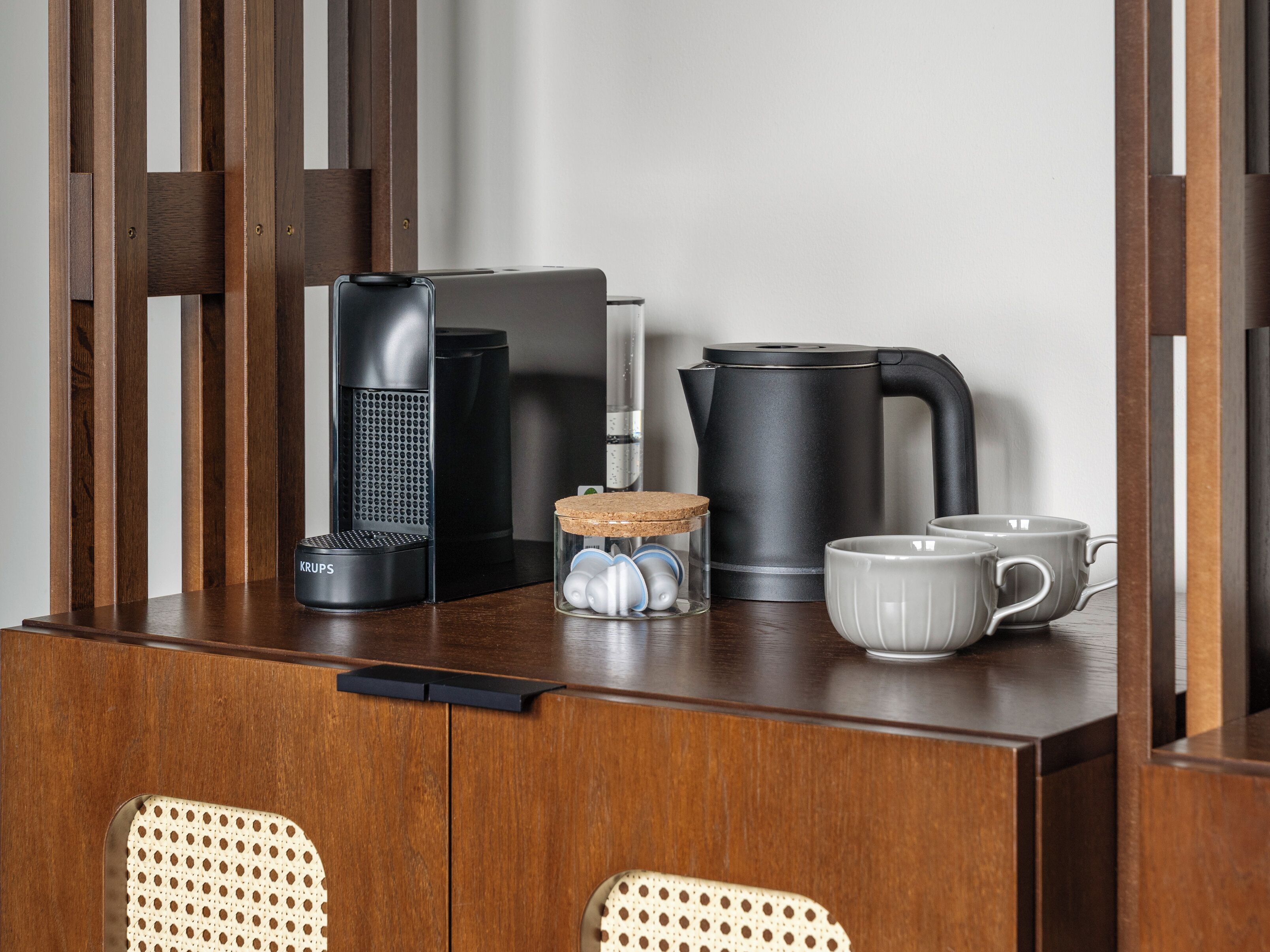 A wooden table with a coffee maker, a kettle, a mug, and a speaker.