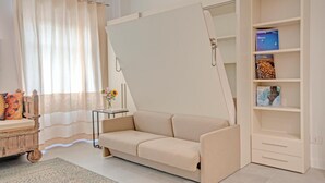 A room with a sofa bed, a small table with a vase of flowers, and a bookshelf. - Right House Sur Le Port (CAGLIARI)