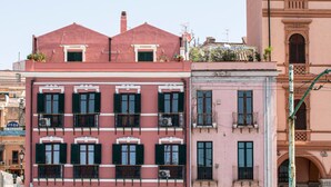 A multi-story building with a pink facade, green shutters, and balconies with wrought iron railings. - Right House Sur Le Port (CAGLIARI)