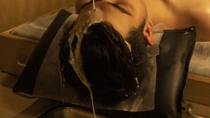 Une personne reçoit un traitement qui consiste à verser un liquide sur sa tête à l’aide d’un grand récipient en métal.