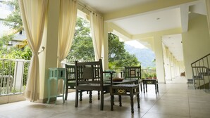 Un espace extérieur abrité, aménagé avec une table et des chaises, une petite table ornée d’un objet décoratif, et offrant une vue sur la verdure et les montagnes en arrière-plan.