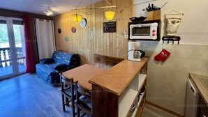 A cozy kitchen with wooden walls, a dining table, chairs, a microwave, and a coffee maker.
