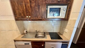 A compact kitchen with a built-in microwave, a sink, a dishwasher, and a compact refrigerator.