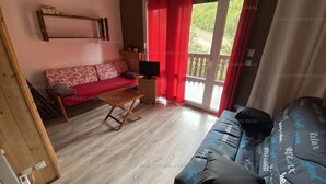 A cozy living room with a red sofa, a wooden coffee table, and a TV stand. - Cozy 2* Apt, Ski-In/Out, Sleeps 4, Balcony, Parking, Near Hot Springs (Les Angles)