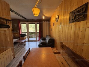 A wooden interior with a dining table, chairs, a sofa, and a balcony with a view.