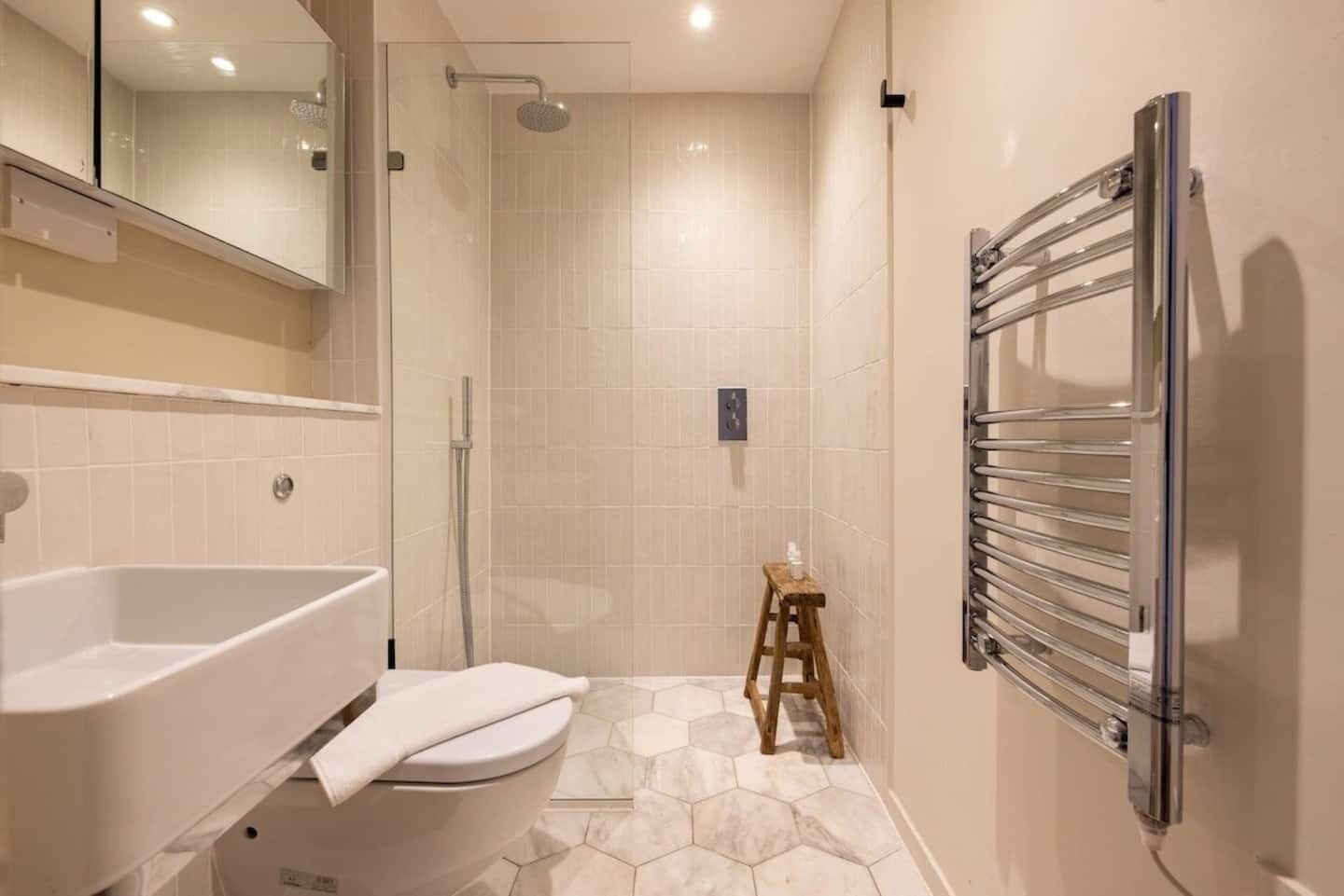 Een moderne badkamer met bad, toilet, douche en een houten kruk.