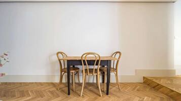 A dining area with a wooden table and chairs, a herringbone-patterned floor, and a white wall.