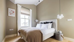 Ein Schlafzimmer mit einem Bett, einem Fenster mit Vorhängen, einem Nachttisch und einer Wandleuchte.