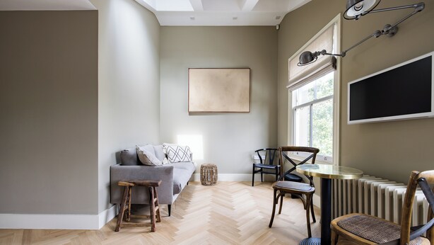 Ein modernes Wohnzimmer mit Fischgrätparkett, einem grauen Sofa, einem runden Tisch und zwei Stühlen.