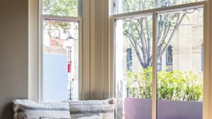 Un siège de fenêtre agrémenté de coussins, un luminaire suspendu et une vue sur un arbre et des bâtiments à l’extérieur.