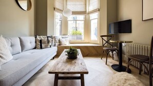 Un salon avec un canapé, une table basse ornée d’une plante, un fauteuil, un téléviseur et un radiateur.