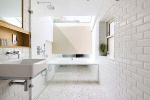 A modern bathroom with a freestanding bathtub, a showerhead, and a small potted plant.