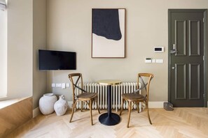 A room with a round table, two chairs, a television, a radiator, a door, and a vase.