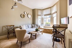 A living room with a sofa, armchairs, a coffee table, and a TV mounted on the wall. - The Notting Hill Apartments by HoK Living - NH2 (Greater London)