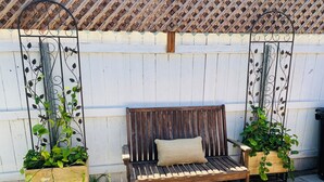 A wooden bench with a cushion, positioned against a white fence with decorative metal elements.