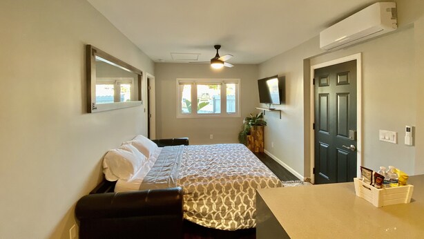 A bedroom with a bed, a desk, a chair, a TV, and a door.