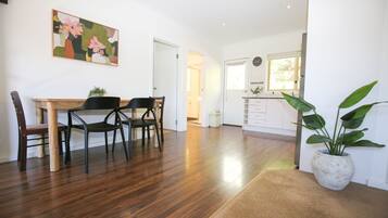 A dining area with a wooden table and chairs, a kitchen with white cabinets, and a potted plant.