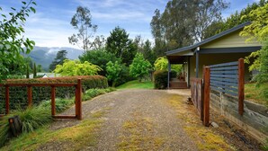Una strada sterrata che conduce a una zona relax all'aperto, riparata, con una recinzione in legno e un edificio con tetto a falde.