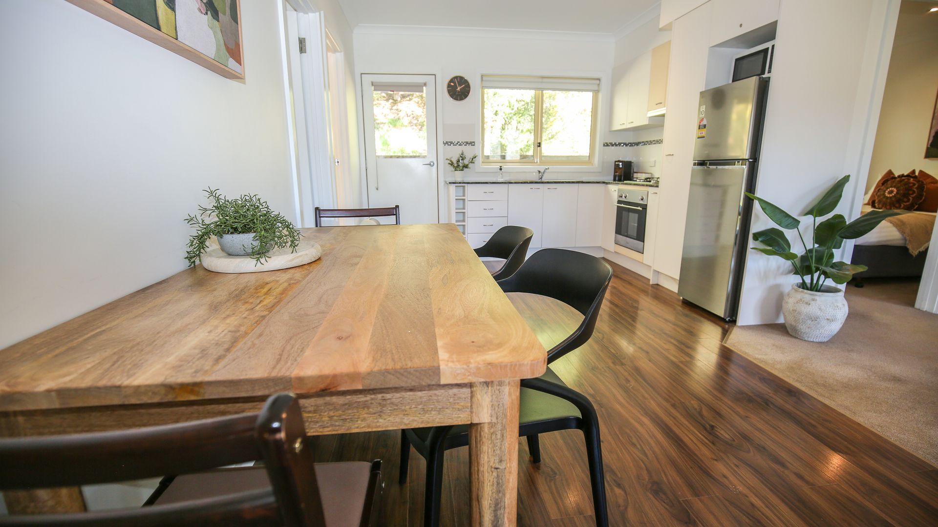 A modern kitchen with a wooden dining table, black chairs, and a stainless steel refrigerator.
