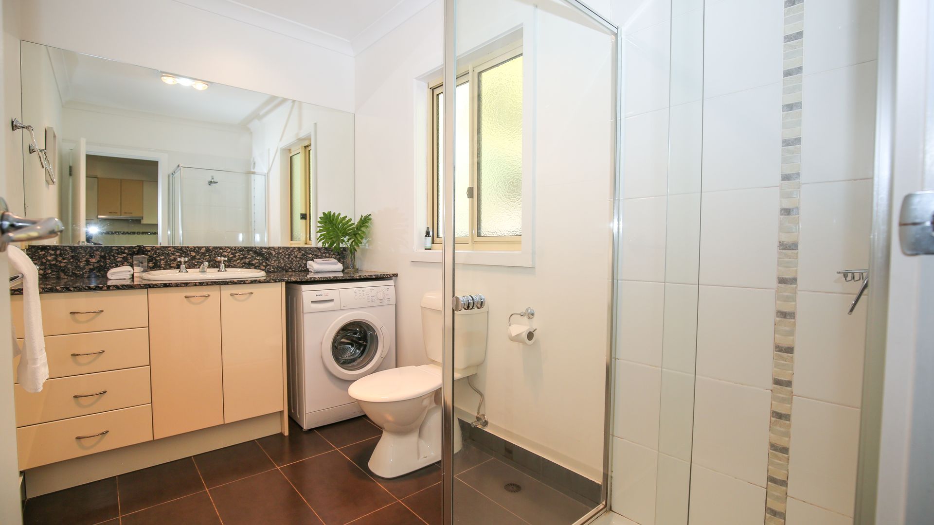 Une salle de bain moderne équipée d’un lave-linge, de toilettes et d’une douche.
