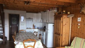 A cozy cabin interior with a dining table, chairs, a sofa, a washing machine, and a kitchen area with cabinets and a refrigerator. - 3* Chalet for 8, fireplace, parking, free shuttle (Les Angles)
