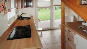 A kitchen with a wooden countertop, a built-in stove, a sink, and a view of a grassy yard through an open door.