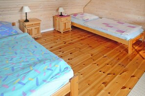A room with two wooden beds, a nightstand with a lamp, and a wooden floor.
