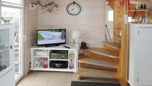 A room with a television on a white stand, a clock on the wall, a staircase, and a door leading outside.
