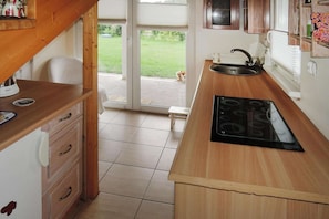 A kitchen with a wooden countertop, a black stove, a sink, and a view of a grassy yard through a glass door.