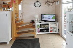 A room with a wooden staircase, a television on a white stand, and a clock on the wall. - Holiday Home on Lake Ostrowo near Baltic Sea (Troszyn)