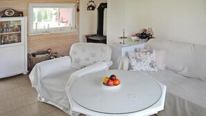 A cozy living room with a white sofa, a round glass table with fruit, a white cabinet with glass doors, and a black stove.