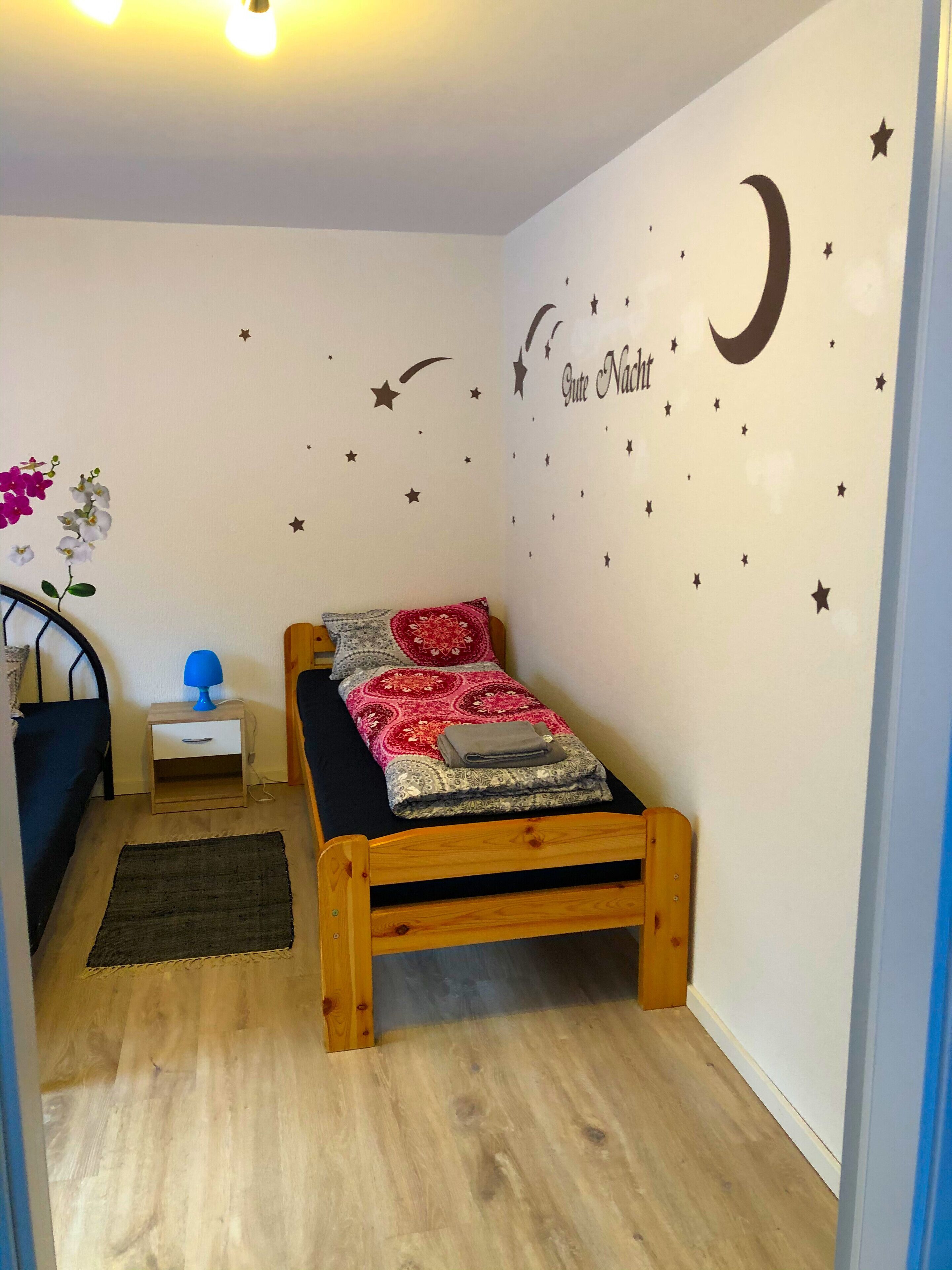 A bedroom with a wooden bed, a night sky wall decal, a small bedside table with a lamp, and a night sky poster.