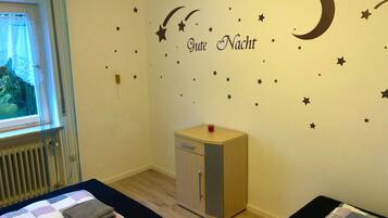 A room with a bed, a small cabinet, and a wall with star and moon decals.