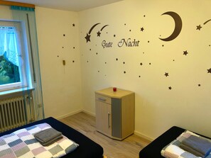 Une pièce comprenant un lit, une petite armoire et un mur décoré d’autocollants représentant des étoiles et une lune.
